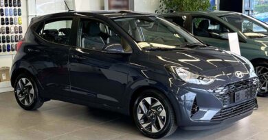 Vista laterale della nuova Hyundai i10 in esposizione in concessionaria, con design compatto, griglia frontale a nido d’ape e cerchi in lega da 16 pollici.